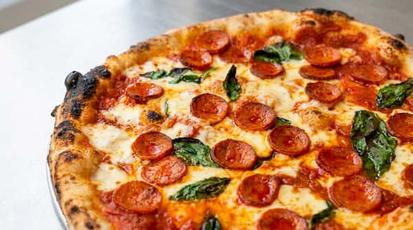 Pepperoni pizza with melted mozzarella, red sauce, green basil, and a charred crust.