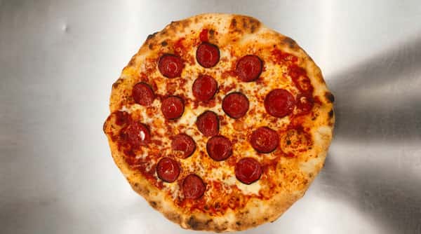 Pepperoni pizza with melted cheese, tomato sauce, and numerous red pepperoni slices on a light background.