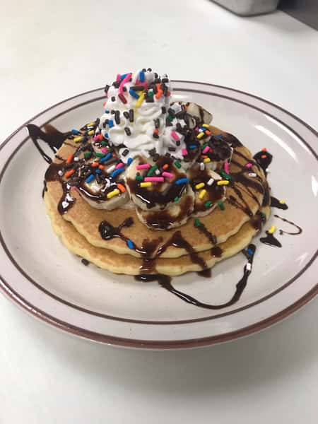 Pancakes topped with bananas, sprinkles, and chocolate syrup