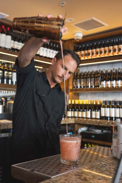 A skilled mixologist at Parlor San Clemente expertly preparing a craft cocktail, showcasing the vibrant colors and fresh ingredients used in their extensive drink menu.