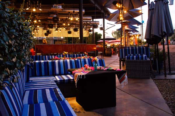 Outdoor patio at O.H.S.O. Party House in Arcadia with blue striped lounge seating, colorful table settings, string lights and covered event space.