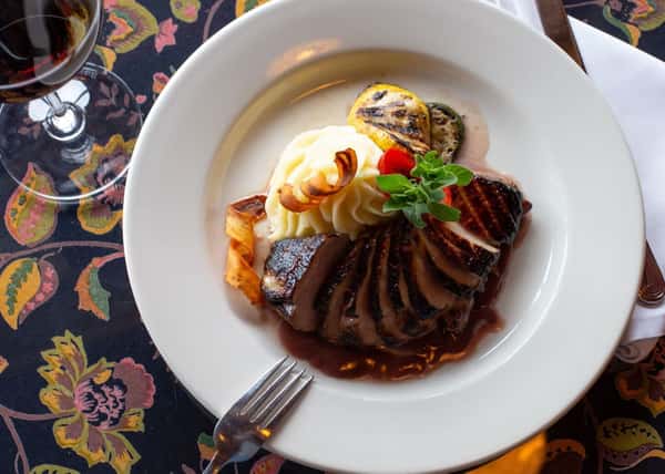 A beautifully plated entrée featuring tender, sliced meat glazed in a rich sauce, served alongside creamy mashed potatoes and vibrant seasonal vegetables for an elegant, hearty presentation.