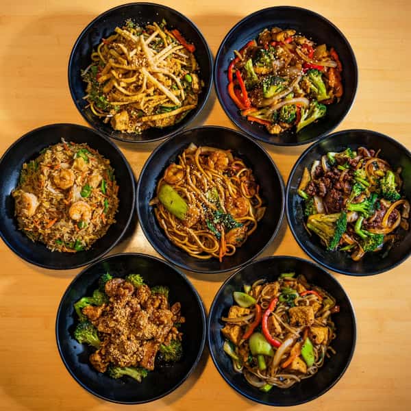 A vibrant assortment of Asian noodle and rice dishes served in black bowls, featuring shrimp, beef, tofu, and fresh vegetables.