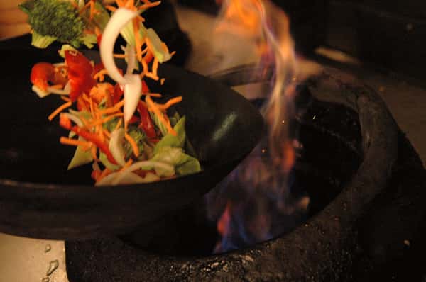 Colorful vegetables being tossed in a wok over an open flame during stir-fry cooking.