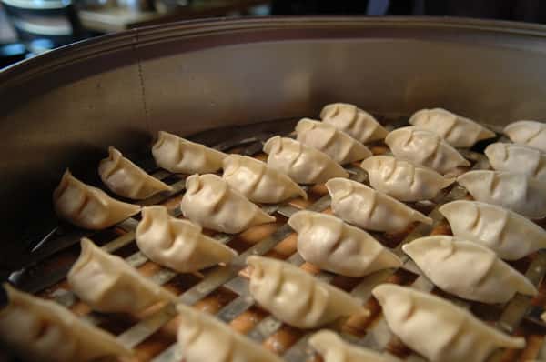 Raw dumplings neatly arranged on a metal rack inside a steamer, ready for cooking in a traditional dim sum preparation.