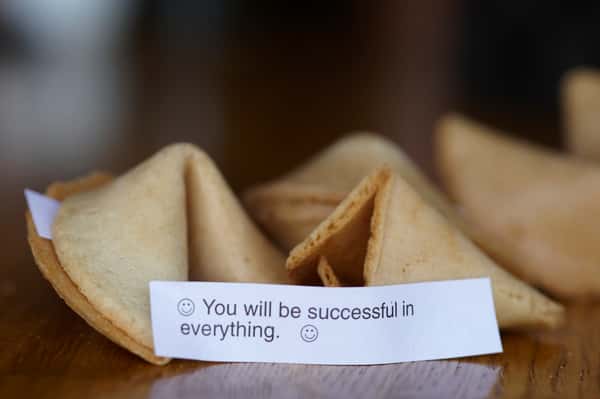 A fortune cookie with a message that reads, "😊 You will be successful in everything. 😊" resting on a wooden surface.