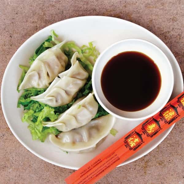 Steamed dumplings served on shredded lettuce with soy dipping sauce and a pair of red chopsticks on the side.