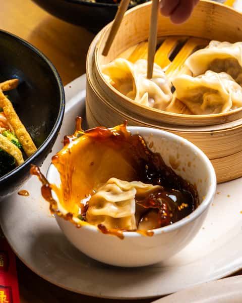 Handmade dumpling splashing into soy dipping sauce