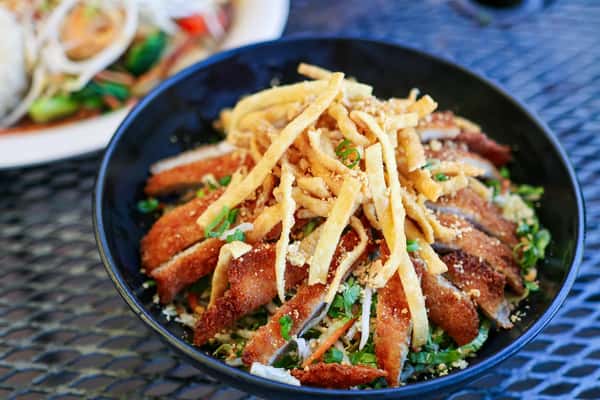 Crispy noodle salad topped with sliced fried meat, chopped scallions, and crushed peanuts served in a black bowl.