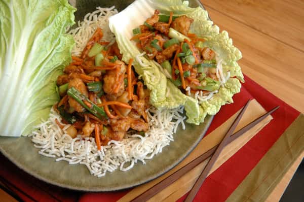Crispy lettuce wraps filled with stir-fried chicken, carrots, scallions, and crunchy rice noodles on a rustic plate with chopsticks.
