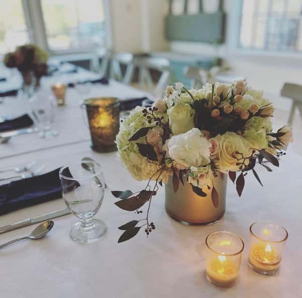 A beautifully set table with soft lighting, featuring a floral centerpiece with white and soft pink roses, surrounded by candles for a warm, intimate atmosphere.