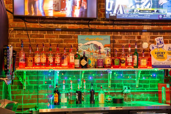 Bar shelves with liquor bottles, neon lighting, and TVs inside The Gaslight Pizza & Grill in Huntingburg, Indiana