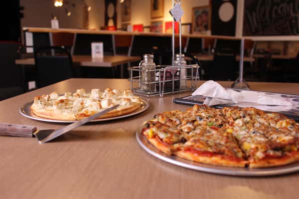 two pizza pies with utensils and menu