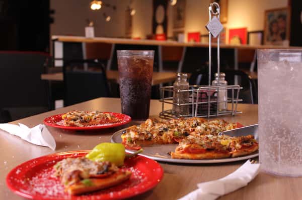 pizza pie with slices on plates and cola