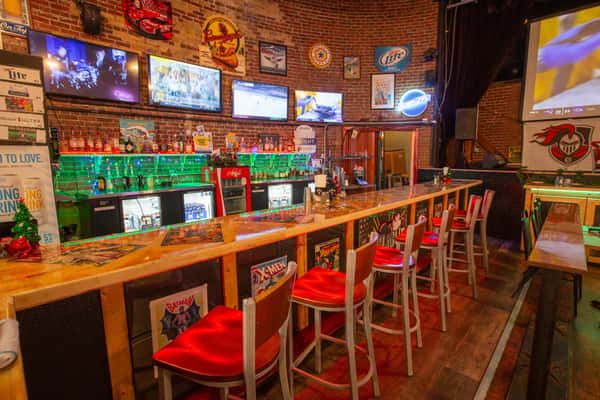 Warm bar interior with TVs, wooden finishes, and red stools at The Gaslight Pizza & Grill in Huntingburg, Indiana