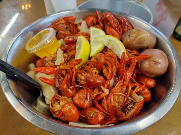 Cajun-style boiled crawfish served in a metal bowl with red potatoes, lemon wedges, onions, and a cup of melted butter, showcasing a casual Southern seafood boil presentation.