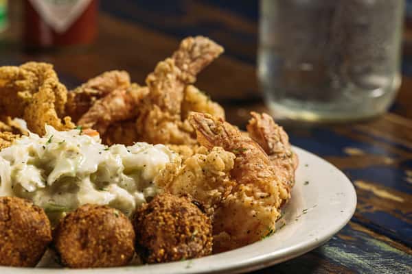 Southern fried seafood platter with crispy fried shrimp, hushpuppies, creamy coleslaw, and seasoned batter, served on a rustic table at a casual seafood restaurant