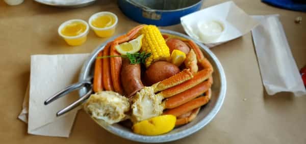 Seafood boil bowl with snow crab legs, corn on the cob, red potatoes, sausage, lemon wedges, and melted butter, served Cajun-style at a Southern seafood restaurant.