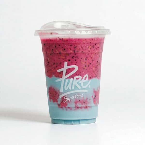 Eye-catching layered smoothie with bright pink dragon fruit blend and pastel blue yogurt swirl, served in a branded Pure Superfood cup.