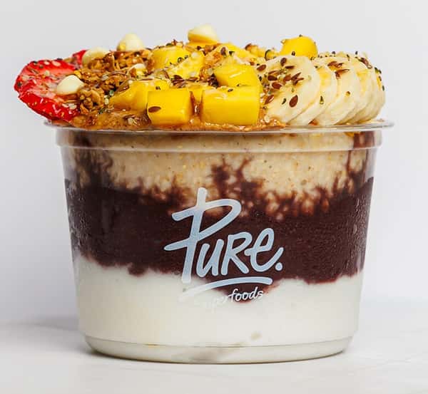 Layered acai bowl from Pure Superfoods with creamy yogurt, rich acai blend, fresh banana, mango chunks, strawberry slices, granola, and flaxseeds.