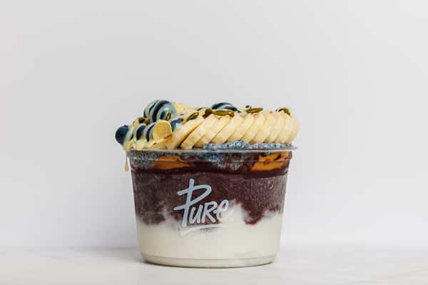 Pure Superfoods acai bowl layered with yogurt, topped with sliced banana, fresh blueberries, chia pudding, and a drizzle of nut butter.