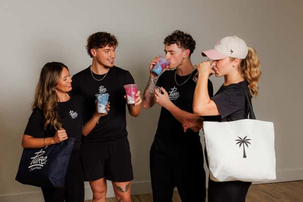 Group of young adults in Pure Superfood gear enjoying colorful smoothies, showcasing the brand's energetic and healthy community vibe.