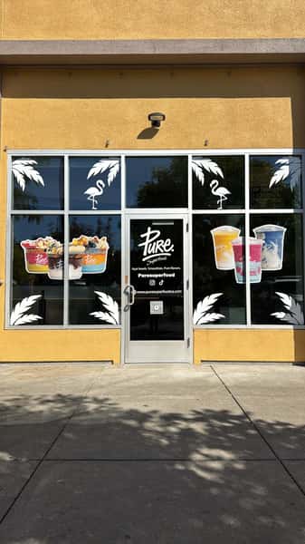 Pure Superfood storefront with window graphics showcasing colorful smoothie bowls and protein-packed drinks against a sunny exterior.