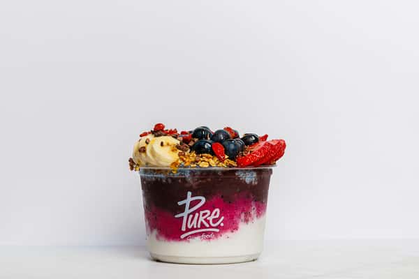 Acai and yogurt bowl from Pure Superfoods topped with sliced banana, strawberries, blueberries, crunchy granola, and goji berries.