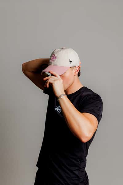 Man wearing a pink and beige Pure Superfood cap and black branded t-shirt, adjusting his hat in a casual lifestyle pose.