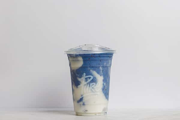 Pure Superfoods layered blue spirulina smoothie with swirls of creamy white yogurt, served in a clear to-go cup with lid.