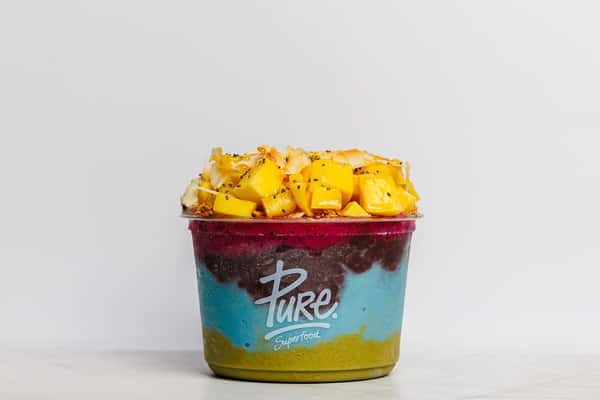 Colorful layered smoothie bowl with green matcha, blue spirulina, acai, and vibrant pink dragon fruit, topped with mango chunks, pineapple, granola, and chia seeds, served in a Pure Superfoods cup.