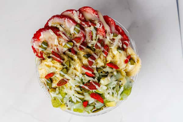 Overhead view of a tropical fruit bowl with sliced strawberries, kiwi, shredded coconut, pumpkin seeds, and goji berries, drizzled with creamy topping.
