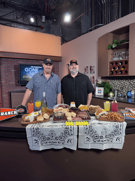 Foley Ranch BBQ team members posing on the Fox 10 Arizona studio set with a spread of smoked barbecue, Southern sides, signature cocktails, and country bar favorites.