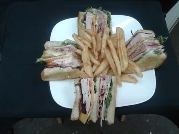 A triple decker of thinly sliced turkey breast, ham, crisp bacon, Swiss and Cheddar cheese, lettuce, tomatoes and mayo served on toasted sourdough with a side of french fries.