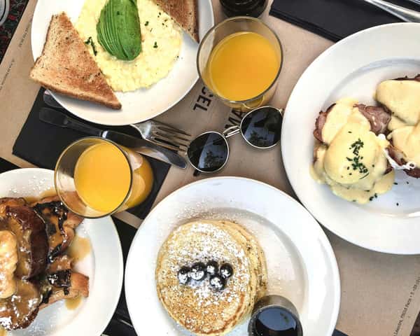 Brunch spread with scrambled eggs and avocado toast, eggs benedict, pancakes with berries, French toast, and orange juice.