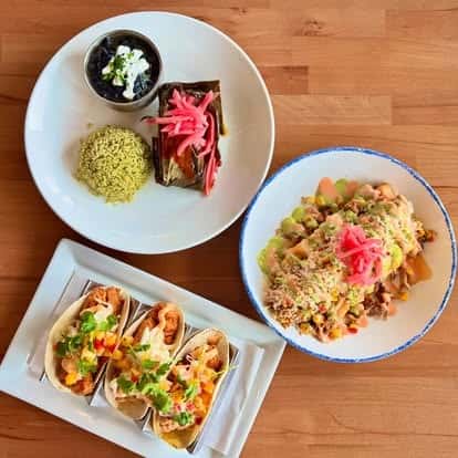 Latin-inspired meal trio featuring grilled chicken tacos, wrapped tamales with green rice and black beans, and a rice bowl topped with pickled onions.