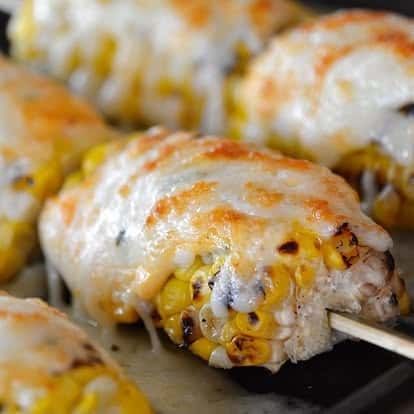 Grilled elote-style Mexican street corn on skewers, smothered in melted cheese and lightly charred for a smoky flavor.