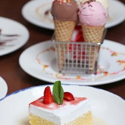 Slice of tres leches cake garnished with strawberries and mint, alongside waffle cones of chocolate and strawberry ice cream — indulgent Latin dessert selection