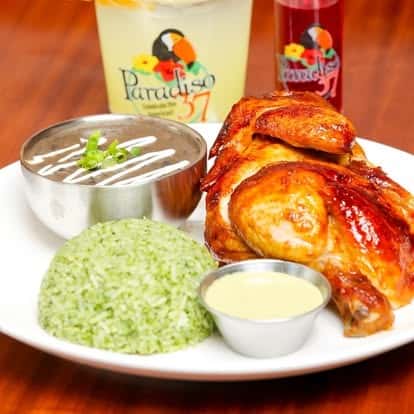 Roasted chicken leg quarter served with cilantro-lime rice, creamy black beans, and a tangy dipping sauce, accompanied by Paradiso 37 specialty drinks.