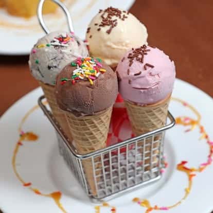 Four colorful ice cream cones in a mini fry basket, featuring chocolate, vanilla, strawberry, and cookies & cream scoops, topped with festive sprinkles.