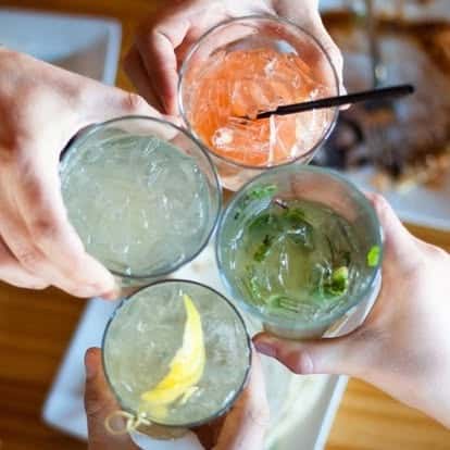 Overhead shot of friends toasting with a variety of colorful cocktails, featuring citrus garnishes and ice, capturing a festive dining atmosphere.