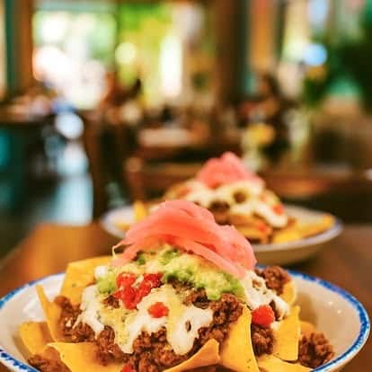 Hearty nachos topped with seasoned ground beef, melted cheese, guacamole, diced tomatoes, and pickled onions — vibrant Mexican appetizer in a festive restaurant setting.
