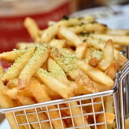 Crispy golden French fries dusted with herb seasoning, served in a metal fry basket for a casual dining presentation.