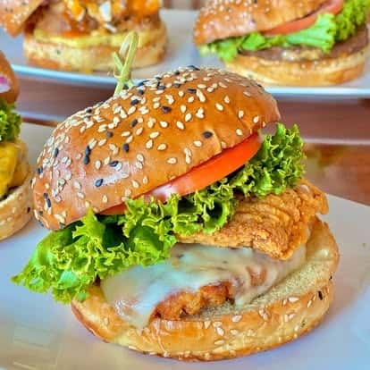 Crispy fried chicken sandwich with melted cheese, leafy green lettuce, and tomato on a toasted sesame seed bun.