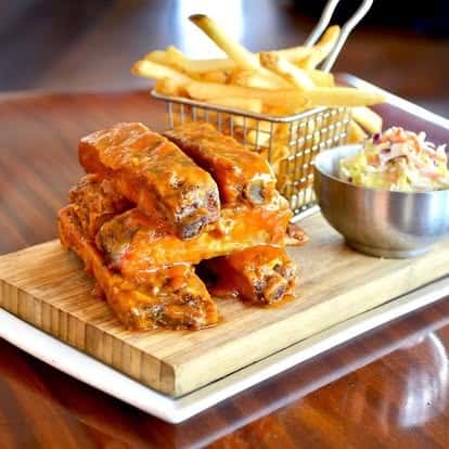 Smoky barbecue pork ribs served with golden French fries in a wire basket and a side of creamy coleslaw on a wooden board.