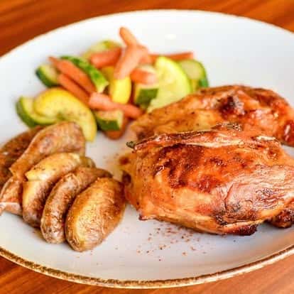 Oven-roasted chicken breast served with sautéed zucchini, carrots, and roasted potato wedges on a rustic white plate.