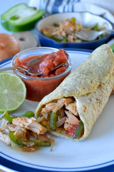 Chicken fajita wrap with sautéed bell peppers and onions, served with salsa and a lime wedge on a white plate.