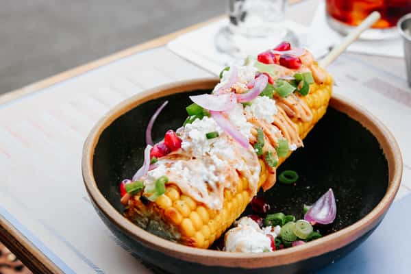 Mexican street corn topped with crema, queso fresco, red onions, pomegranate seeds, green onions, and chili powder.