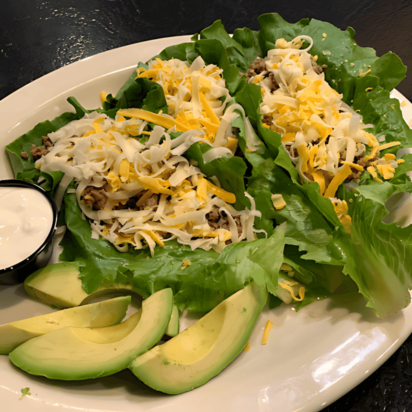 Lettuce wrap tacos filled with ground meat and shredded cheese, served with avocado slices and a side of sour cream.