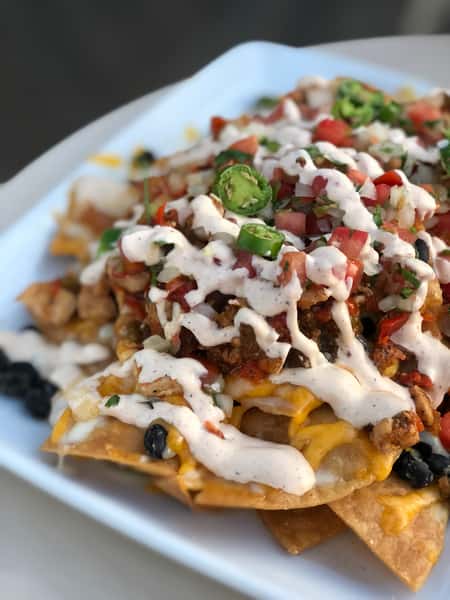 Loaded nachos topped with melted cheese, black beans, pico de gallo, sliced jalapeños, and drizzled with creamy white sauce.